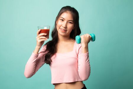 Young healthy Asian woman with dumbbell and  tomato juice on cyan backgroundの写真素材
