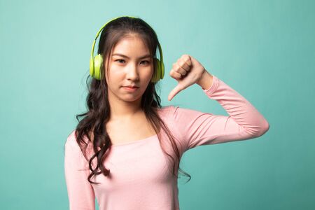 Asian girl don't like  music show thumb down with her headphones on cyan backgroundの写真素材