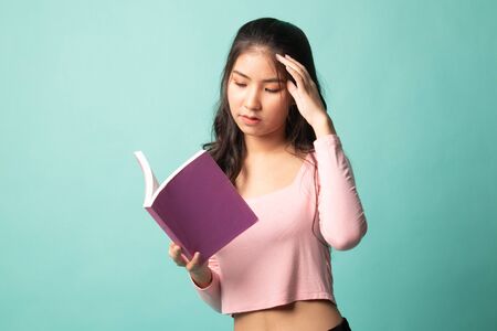 Young Asian woman got headache read a book on cyan backgroundの写真素材