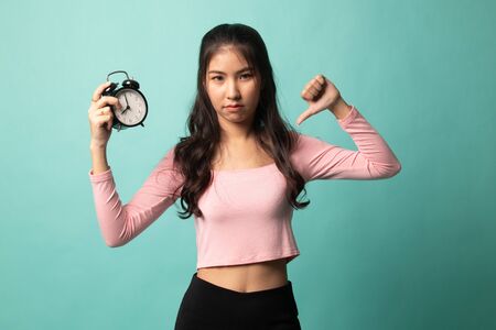 Young Asian woman thumbs down with a clock on cyan backgroundの写真素材