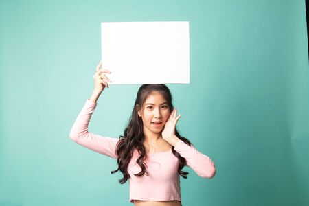 Young Asian woman surprise with white blank sign on cyan backgroundの写真素材