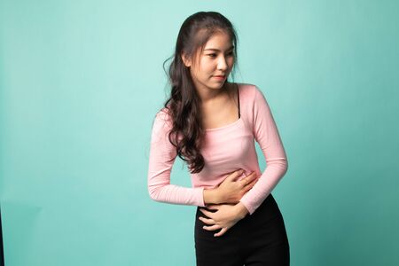 Young Asian woman got stomachache on cyan backgroundの写真素材
