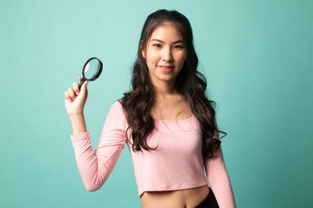 Young Asian woman with a magnifying glass on cyan backgroundの写真素材
