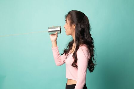 Young Asian woman with tin can phone on cyan backgroundの写真素材