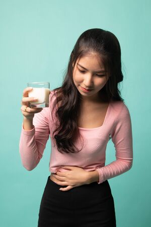 Asian woman drinking a glass of milk got stomachache on cyan backgroundの写真素材