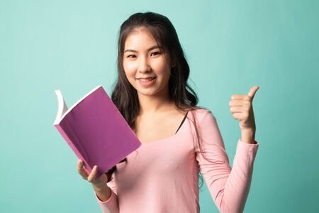Young Asian woman thumbs up with a book on cyan backgroundの写真素材