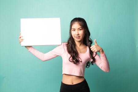 Young Asian woman show thumbs up with  white blank sign on cyan backgroundの写真素材