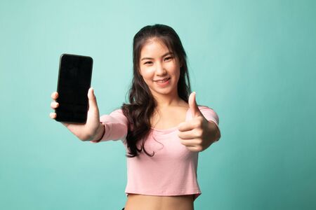 Young Asian woman show thumb up  with mobile phone on cyan backgroundの写真素材