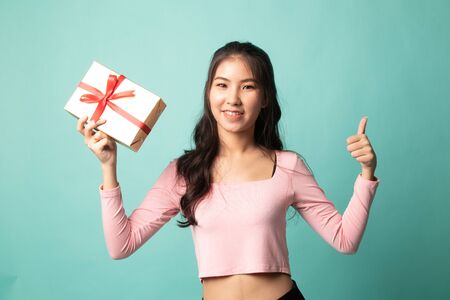 Asian woman thumbs up with a gift box on cyan backgroundの写真素材