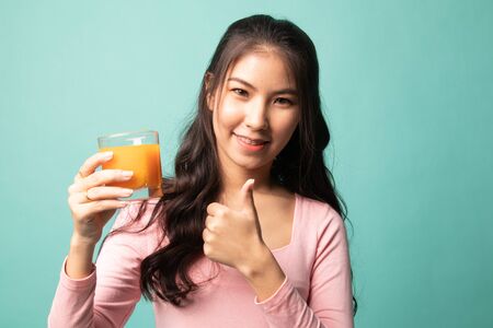 Young Asian woman thumbs up drink orange juice on cyan backgroundの写真素材