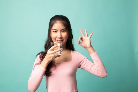 Young Asian woman show OK with a glass of drinking water on cyan backgroundの写真素材