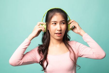 Too loud.  portrait of  young asian woman  holding  headphones and making unhappy face on cyan backgroundの写真素材
