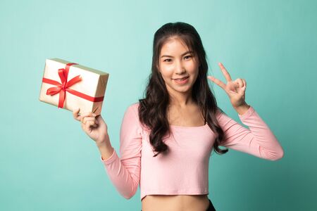 Asian woman show victory sign with a gift box on cyan backgroundの写真素材
