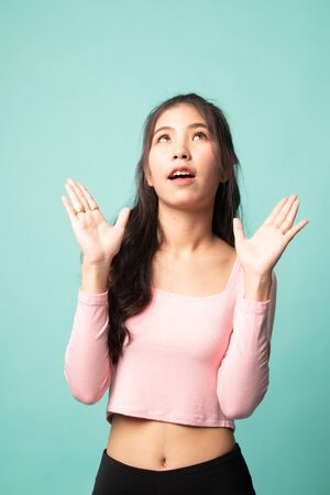 Excited young Asian woman look up on cyan backgroundの写真素材