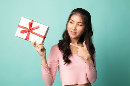 Young Asian woman with a gift box on cyan backgroundの写真素材