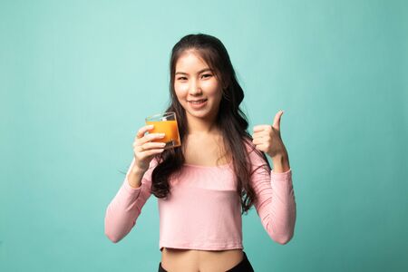 Young Asian woman thumbs up drink orange juice on cyan backgroundの写真素材