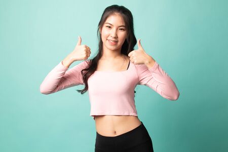 Young Asian woman show two thumbs up on cyan backgroundの写真素材