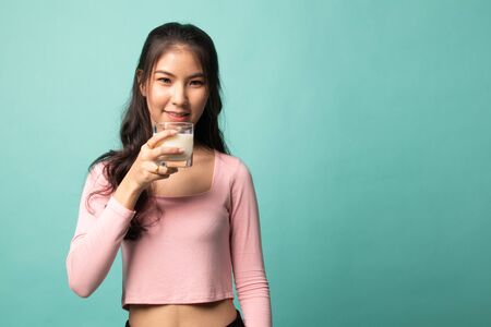 Healthy Asian woman drinking a glass of milk on cyan backgroundの写真素材