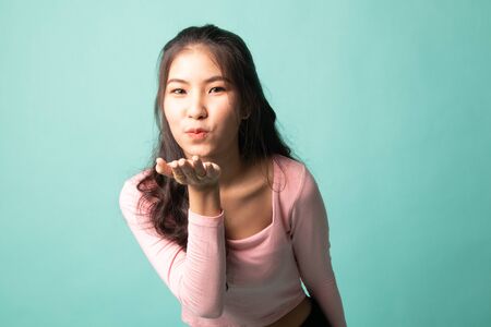 Beautiful young Asian woman blow a kiss on cyan backgroundの写真素材