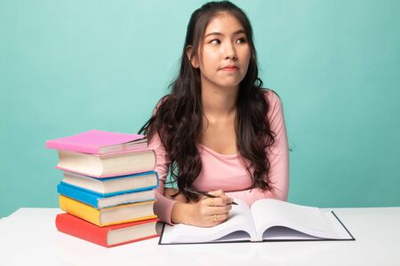 Young Asian woman read a book with books on table on cyan backgroundの写真素材