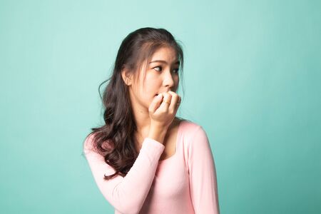 Unsure hesitant nervous young asian  woman biting her fingernails on cyan backgroundの写真素材