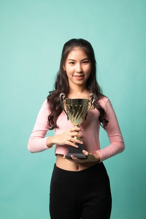 Successful young asian woman holding a trophy on cyan backgroundの写真素材