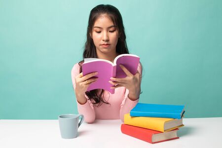 Young Asian woman read a book with cup of coffee on cyan backgroundの写真素材