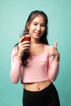 Young Asian woman thumbs up with tomato juice on cyan background