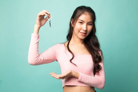 Cute asian girl showing home residence keys on cyan backgroundの写真素材