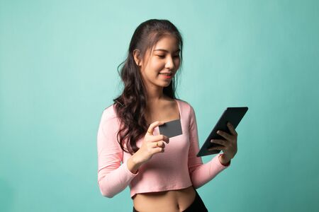 Young Asian woman is shopping online with credit card and tablet on cyan backgroundの写真素材