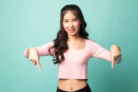 Beautiful young Asian woman point down to blank space on cyan backgroundの写真素材