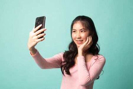 Young Asian woman selfie with mobile phone on cyan backgroundの写真素材