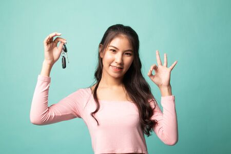 Cute asian girl showing car key on cyan backgroundの写真素材