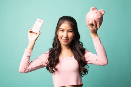 Asian woman with calculator and piggy bank on cyan backgroundの写真素材