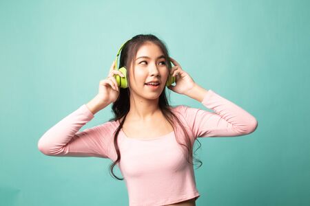 Pretty asian girl listening music with her headphones on cyan backgroundの写真素材