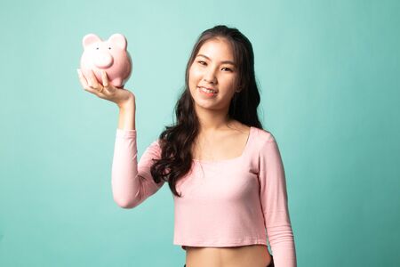 Young Asian woman with a pig coin bank on cyan backgroundの写真素材