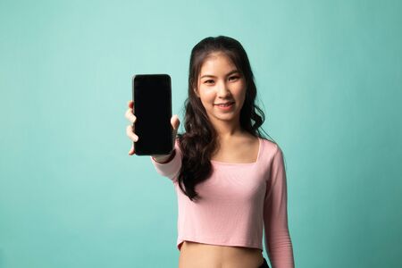 Young Asian woman with mobile phone on cyan backgroundの写真素材