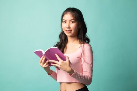 Young Asian woman read a book on cyan backgroundの写真素材