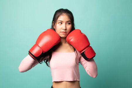 Young Asian woman with red boxing gloves on cyan backgroundの写真素材