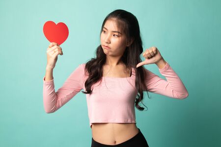 Asian woman thumbs down with red heart on cyan backgroundの写真素材