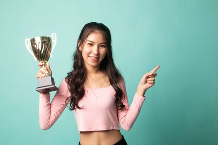 Successful young asian woman holding a trophy point to blank space on cyan backgroundの写真素材