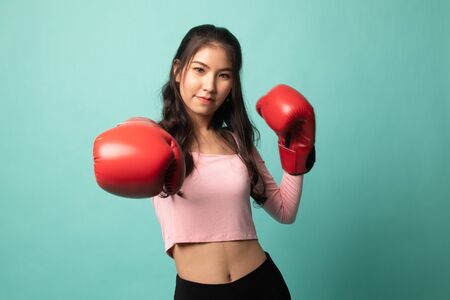 Young Asian woman with red boxing gloves on cyan backgroundの写真素材