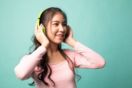 Pretty asian girl listening music with her headphones on cyan backgroundの写真素材