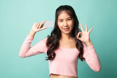 Young Asian woman show OK with a blank card on cyan backgroundの写真素材
