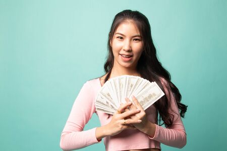 Portrait of  young asian woman  showing bunch of money banknotes on cyan backgroundの写真素材