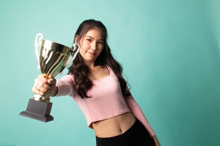 Successful young asian woman holding a trophy on cyan backgroundの写真素材