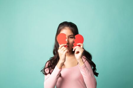 Beautiful young Asian woman with broken heart on cyan backgroundの写真素材