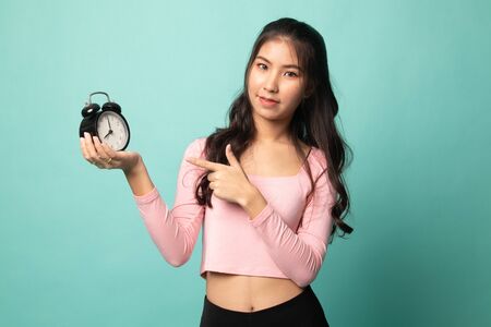 Young Asian woman point to a clock on cyan backgroundの写真素材