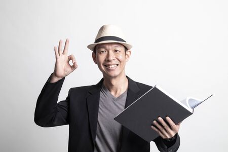 Adult Asian man show OK with a book on white backgroundの写真素材