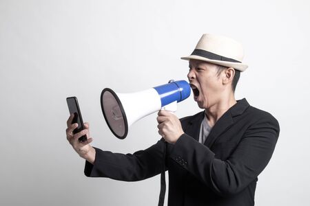 Angry adult Asian man  shout with megaphone to mobile phone on white backgroundの写真素材